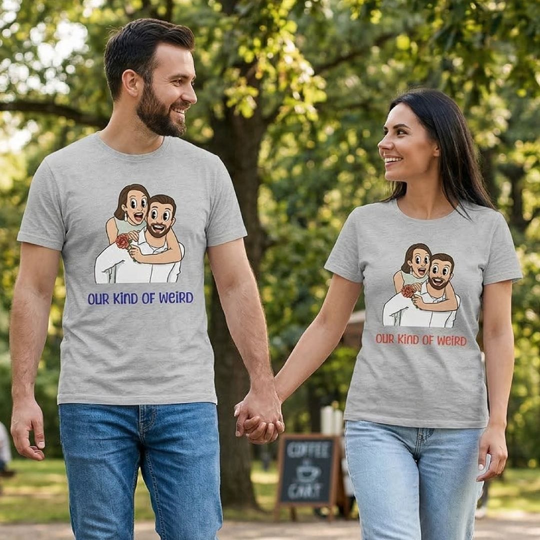 Man and woman holding hands wearing matching t-shirts with a cartoon design and text in a park.